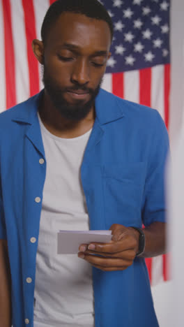 Vertical-Video-Shot-Of-Man-Next-To-Booth-With-Ballot-Paper-In-American-Election-Deciding-How-To-Cast-His-Vote